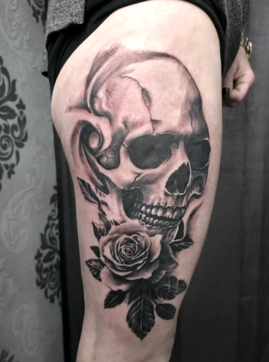 Realistisches Black-&-Grey-Tattoo eines Totenkopfs mit Rose auf dem Oberschenkel.
