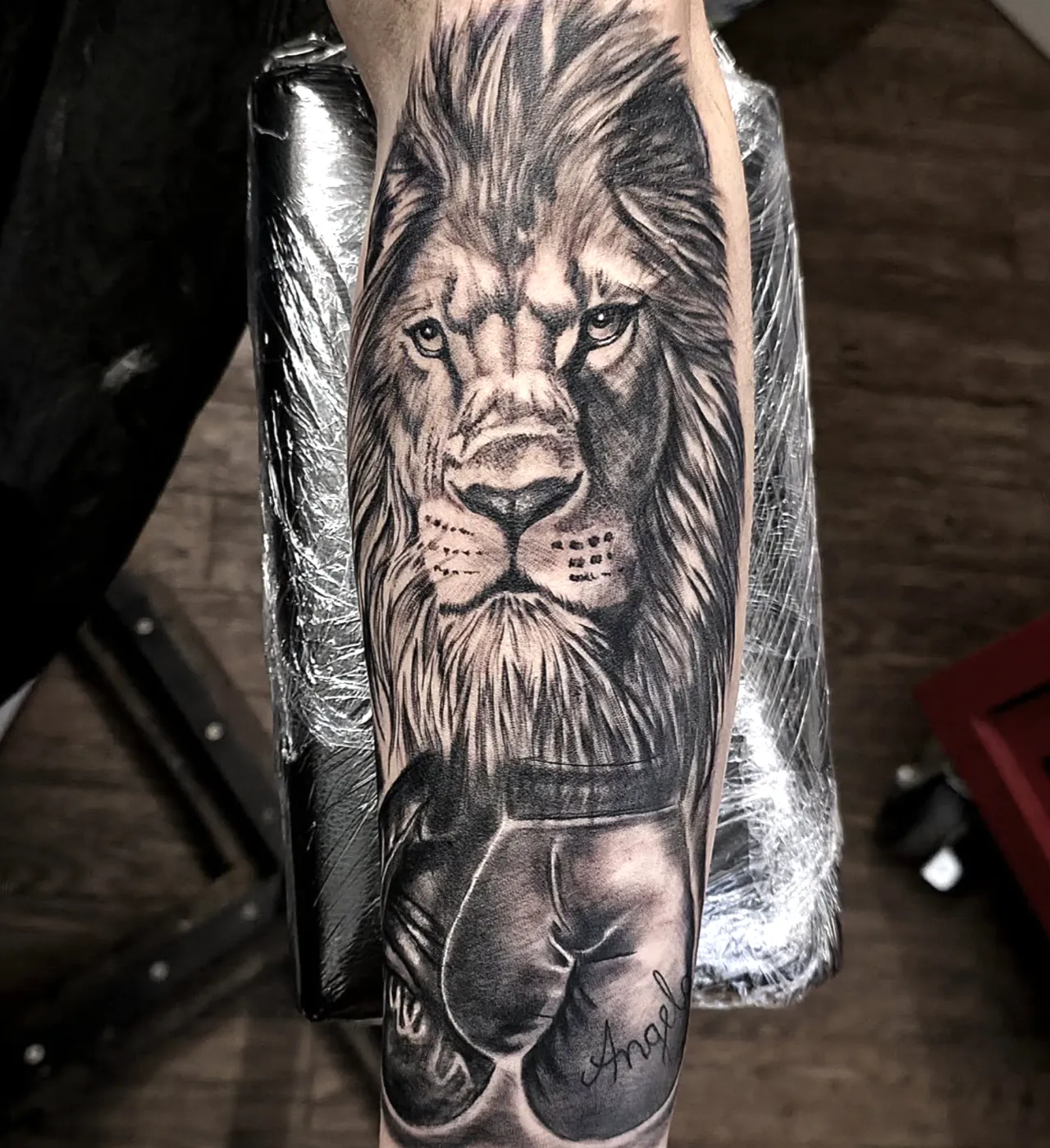 Fotorealistisches Löwenportrait mit Boxhandschuh als Unterarm-Tattoo in Schwarz-Grau.