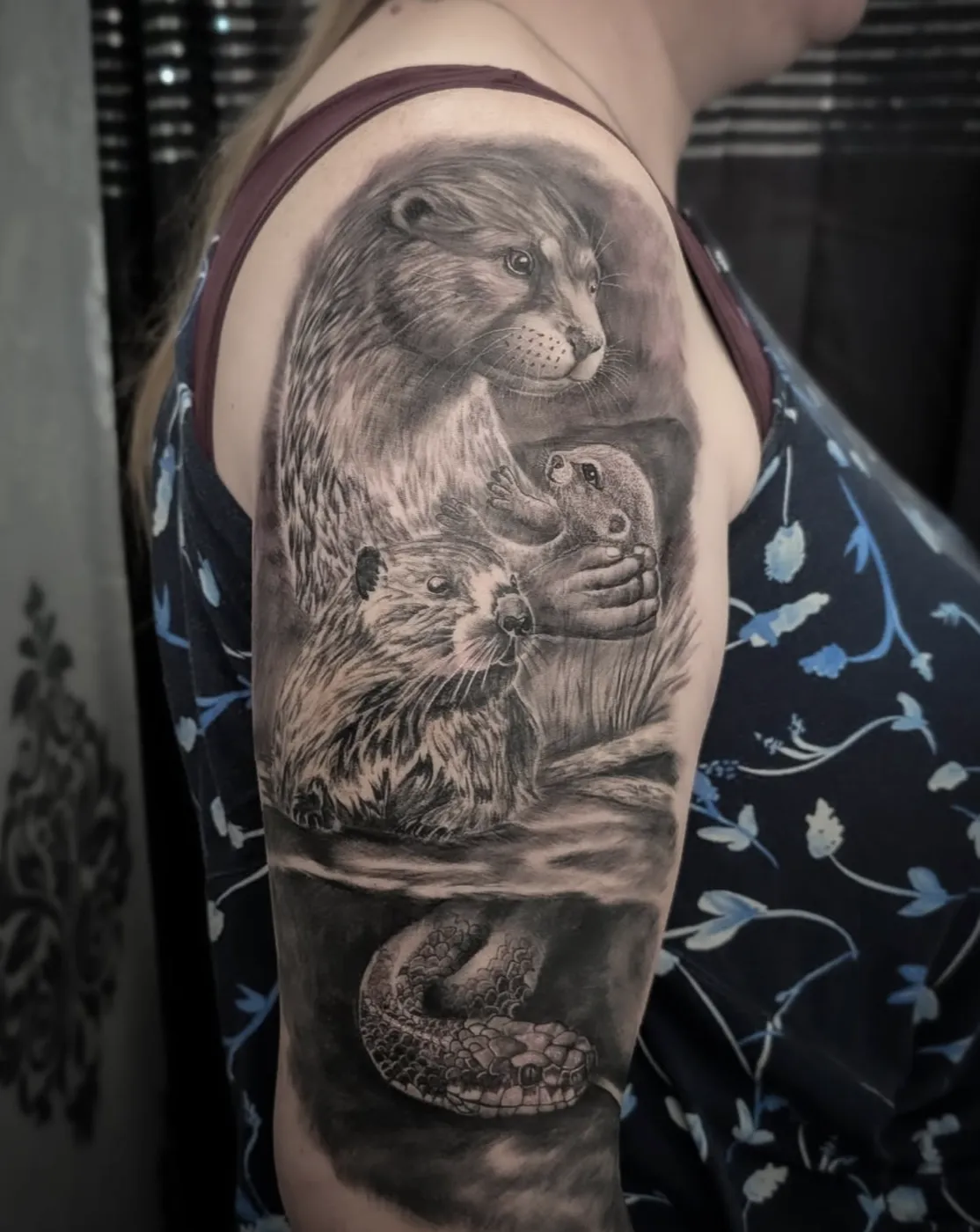 Detailreiches realistisches Tattoo einer Otterfamilie mit Jungtier und Schlange am Oberarm.