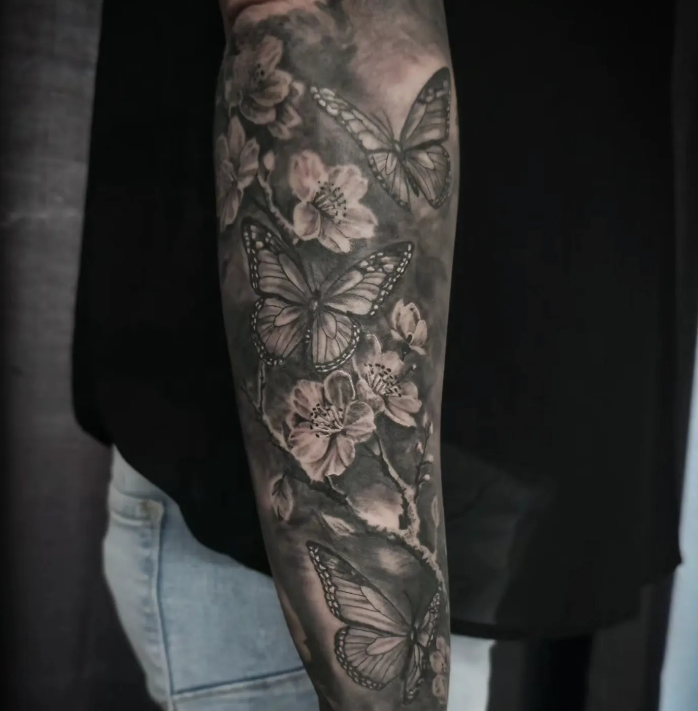 Realistisches Unterarm-Sleeve mit Kirschblüten und Schmetterlingen in feinem Schwarz-Grau.