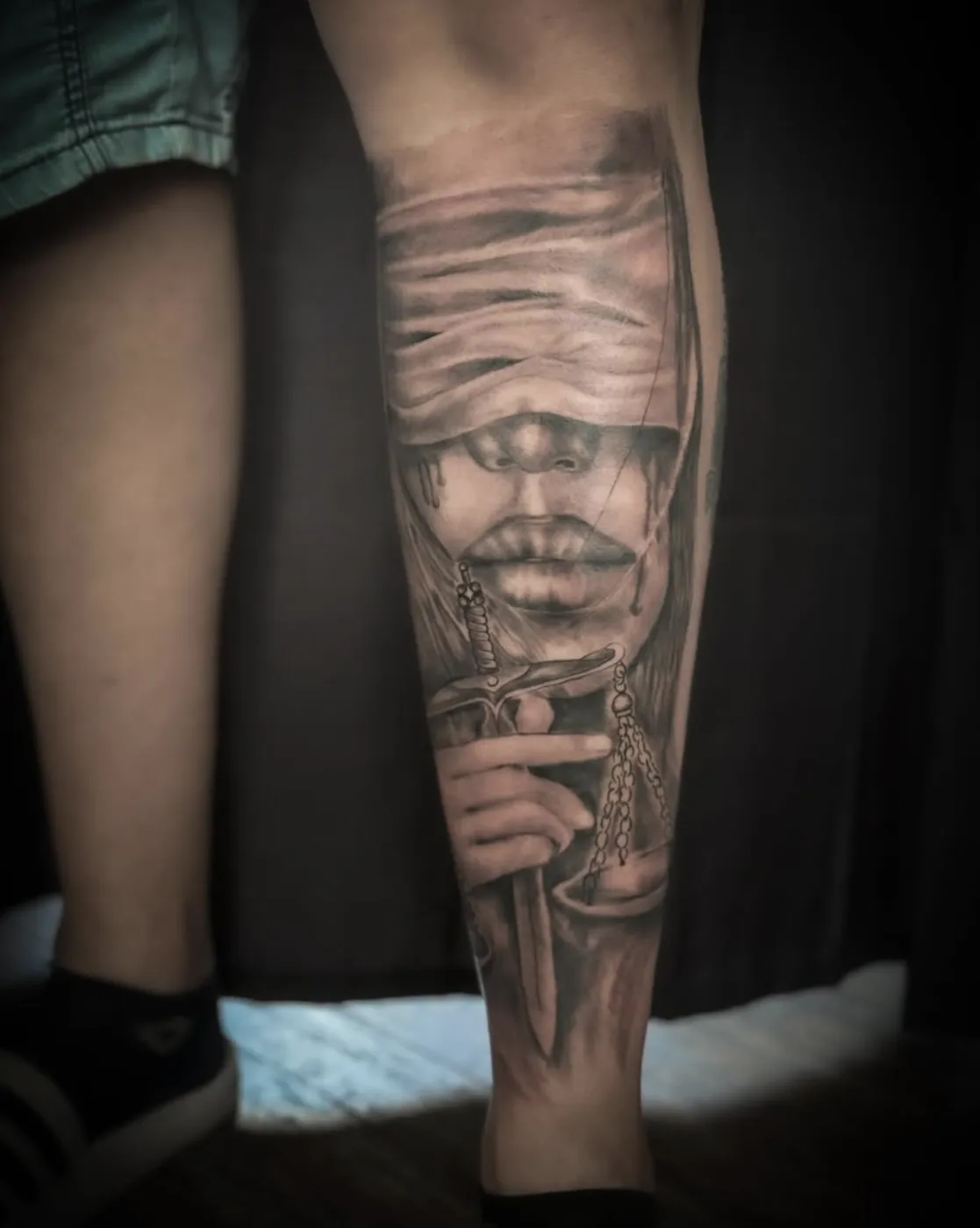 Realistisches Tattoo der Justitia mit Schwert und Waage an der Wade in Schwarz-Grau.