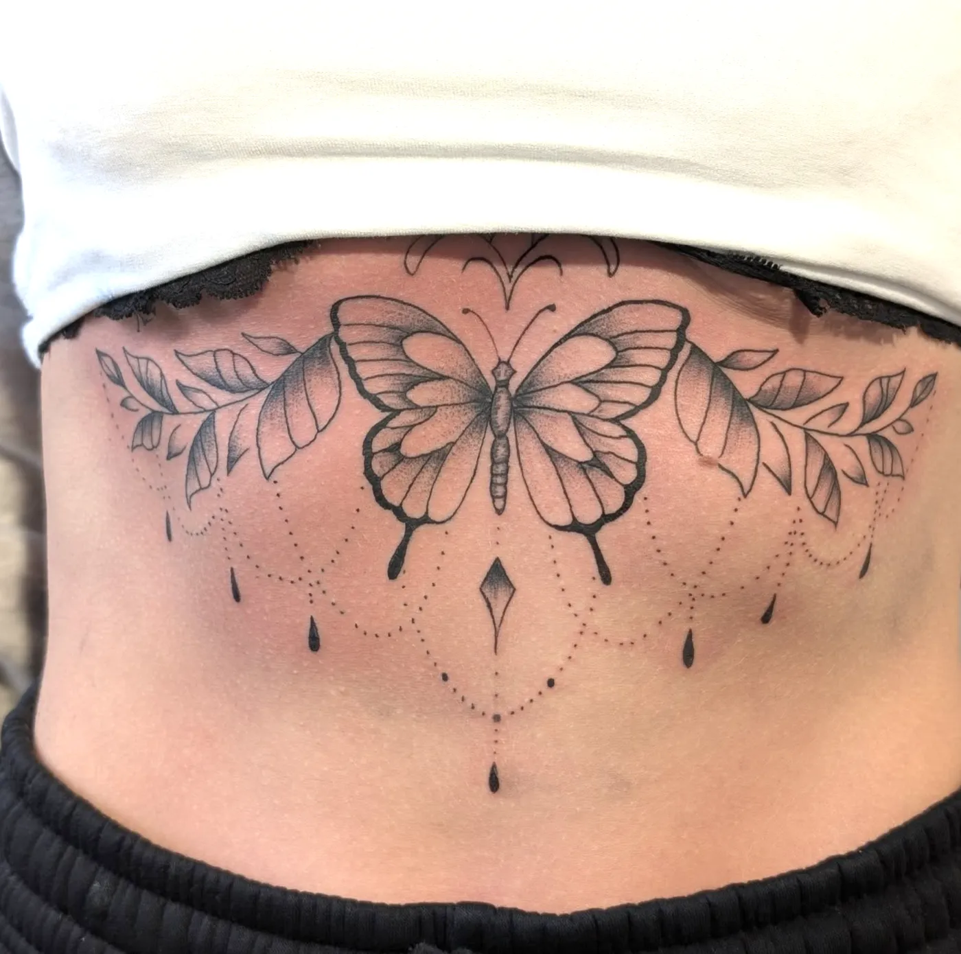 Feines Schmetterling-Sternum-Tattoo mit Ornamenten unter der Brust.